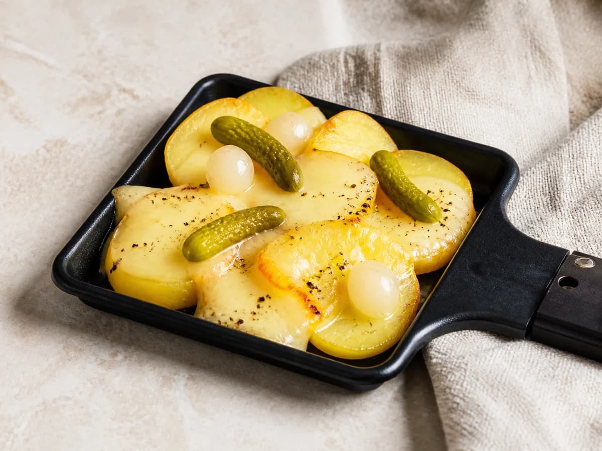 Raclette-Pfännchen mit Kartoffeln, Speck, Käse und Cornichons